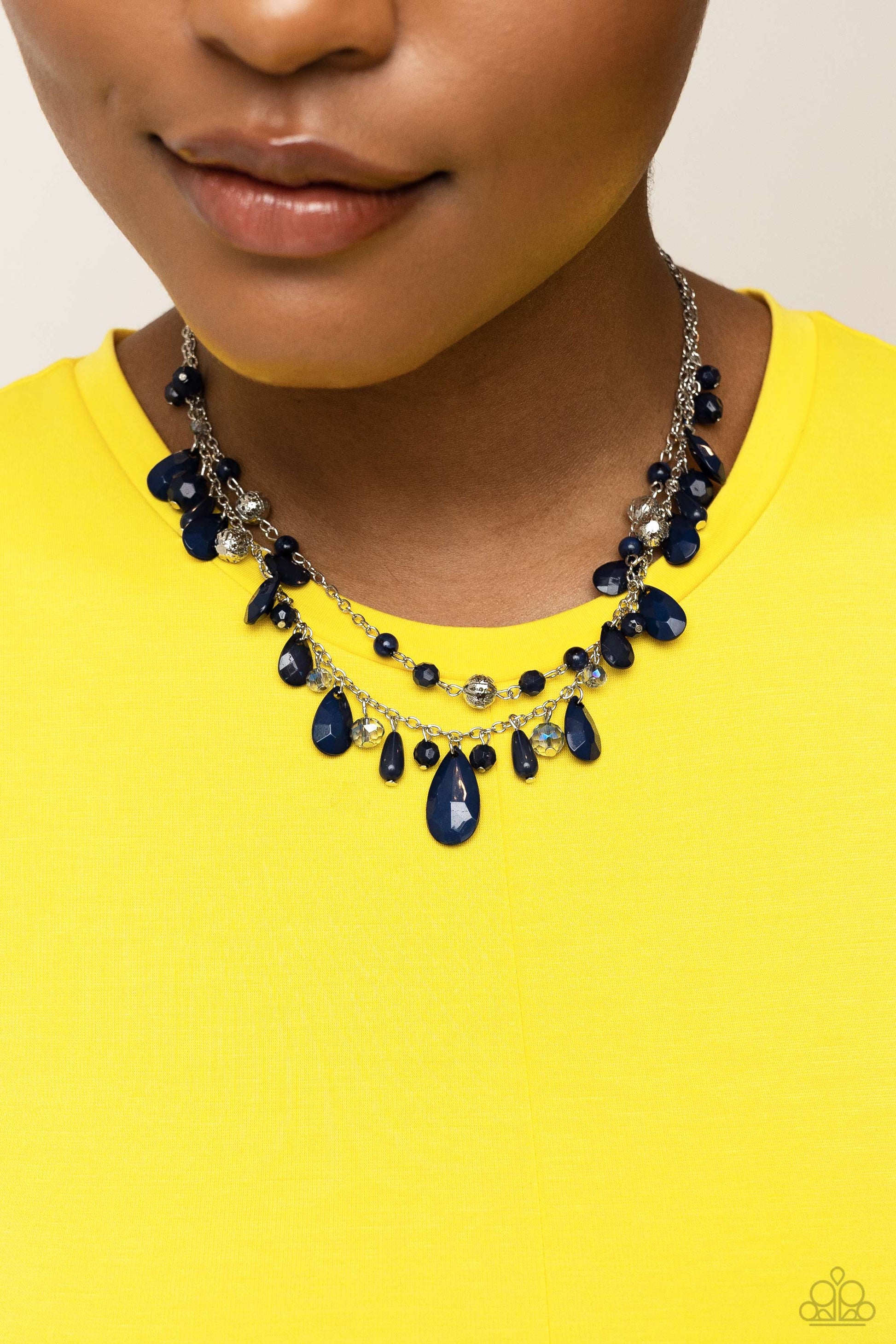 boisterous collection of blue teardrop and round beads, textured silver accents, and faceted blue crystal-like beads trickle from a double strand of silver chain, resulting in flirtatious layers down the neckline. Features an adjustable clasp closure. A dainty collection of blue teardrop and round beads, textured silver accents, and faceted blue crystal-like beads trickle from a single strand of silver chain, resulting in a cheekily clustered chandelier. Earring attaches to a standard fishhook fitting.