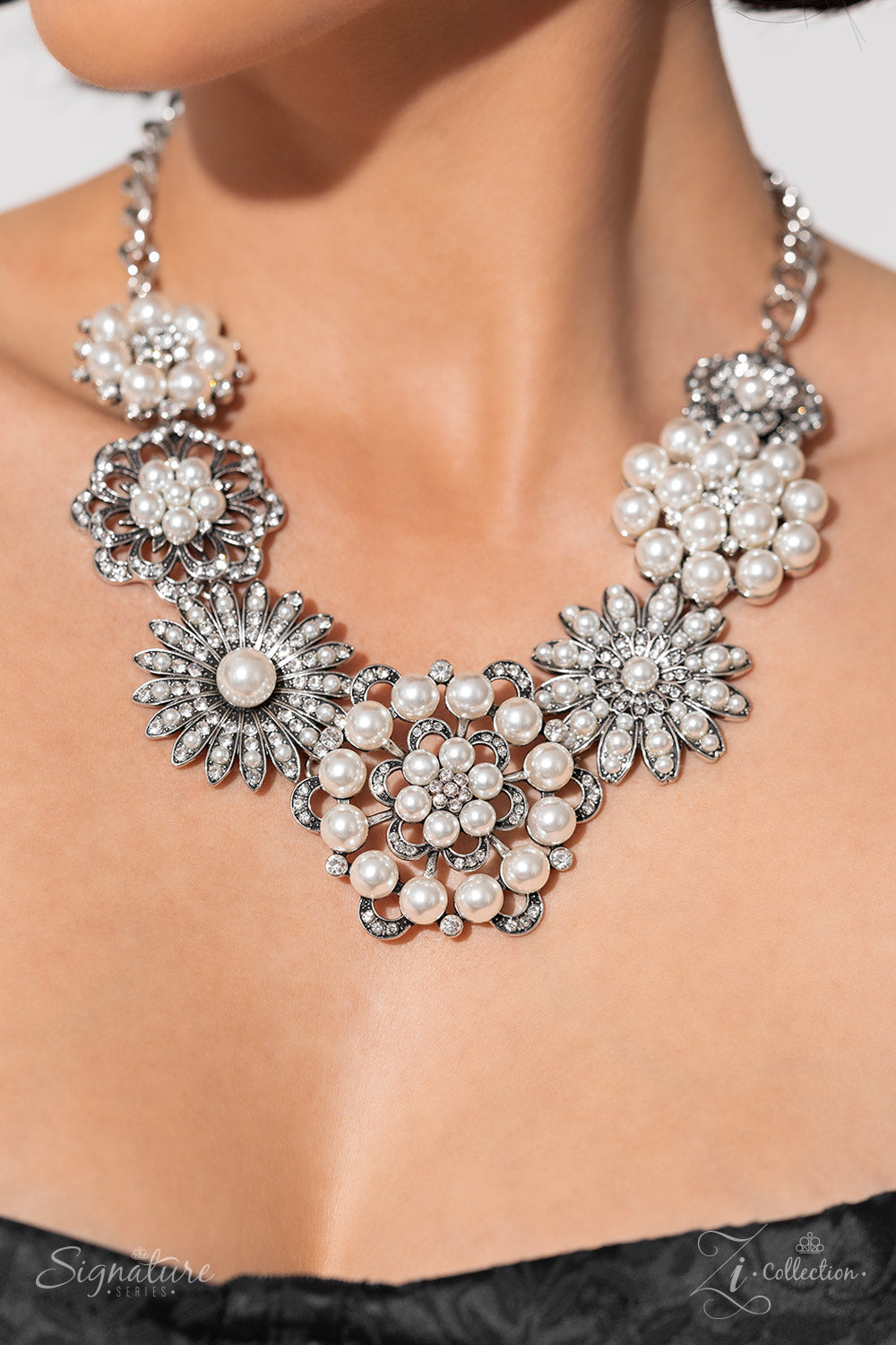Polished white pearls and brilliant white rhinestones bloom atop a framework of silver, forming seven unique flowers adorned in dizzying detail. Each flower features a unique centerpiece encircled by silver petals lined with luminescence and intricate detail. The flourish of florals links whimsically along the neckline, resulting in an unforgettable statement piece that sparkles with sentiment. Features an adjustable clasp closure. Sold as one individual necklace. Includes one pair of matching earrings.