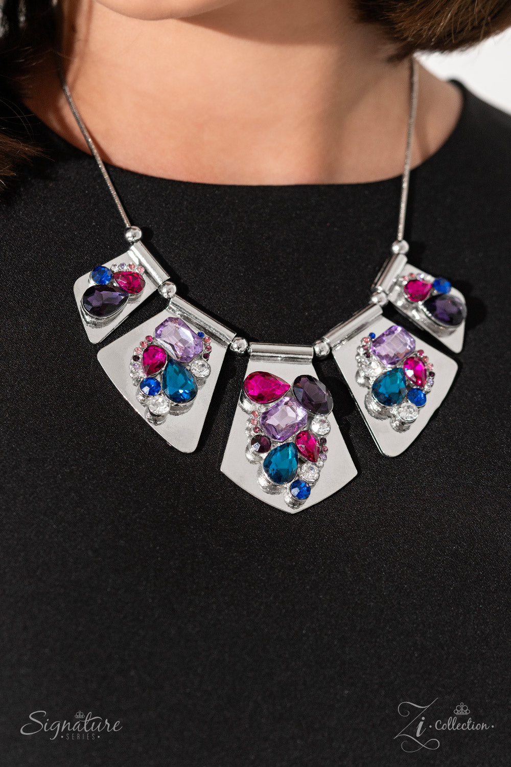 Shimmery silver plates slide along a skinny snake chain, with sleek metallic beads separating each one. Clusters of faceted gems are haphazardly staggered across the surface of each silver canvas, emitting a treasure trove of twinkle in rich shades of blue, purple, and pink. The size and intensity of each elevated grouping become more elaborate as the plates taper to a point at the center of the neckline, resulting in a kaleidoscopic collision of three-dimensional texture and sheen.