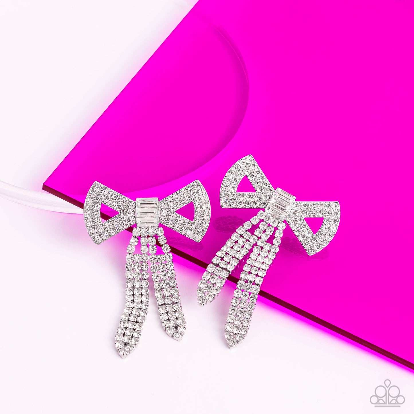 Paparazzi Accessories - Just BOW With It - White Earrings featuring silver square fittings, high-sheen bands of silver, adorned in sparkling white rhinestones loop into a stunning bow charm, creating a classy statement at the ear. Featured in the center of the classy design, a trio of emerald-cut white gems tie the bow together emitting further sheen and glitz. Earring attaches to a standard post fitting. Sold as one pair of post earrings.