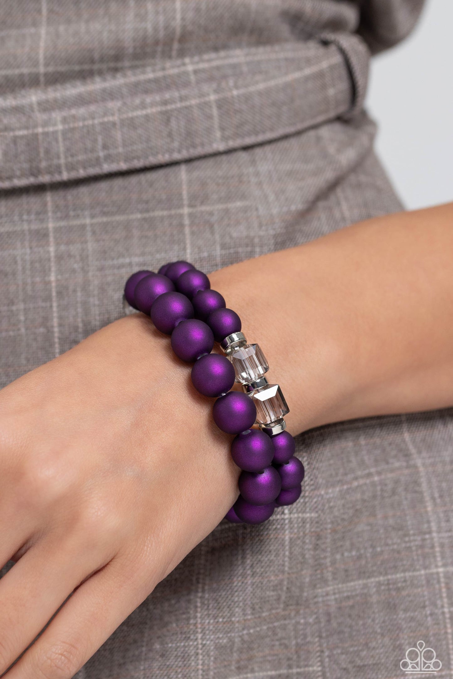 two rows of oversized purple beads featuring a subtle shimmer, silver accents, and clear gray cubed beads fall below the collar on silver paperclip chains, creating refined, colorful layers. Features an adjustable clasp closure. Sold as one individual necklace. Includes one pair of matching earrings. Two strands of oversized purple beads featuring a subtle shimmer, silver accents, and clear gray cubed beads stretch around the wrist, creating refined, colorful layers.