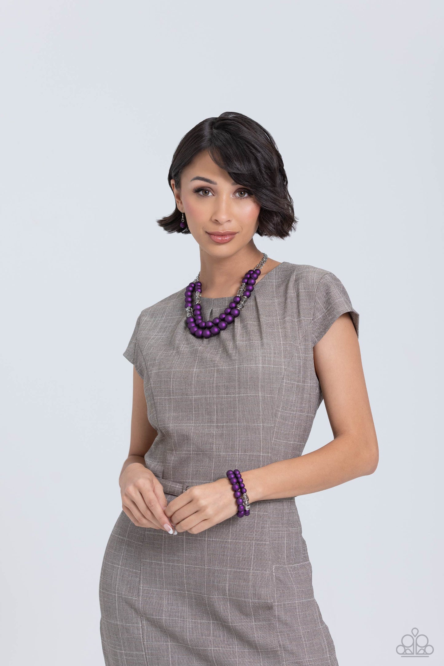two rows of oversized purple beads featuring a subtle shimmer, silver accents, and clear gray cubed beads fall below the collar on silver paperclip chains, creating refined, colorful layers. Features an adjustable clasp closure. Sold as one individual necklace. Includes one pair of matching earrings. Two strands of oversized purple beads featuring a subtle shimmer, silver accents, and clear gray cubed beads stretch around the wrist, creating refined, colorful layers.