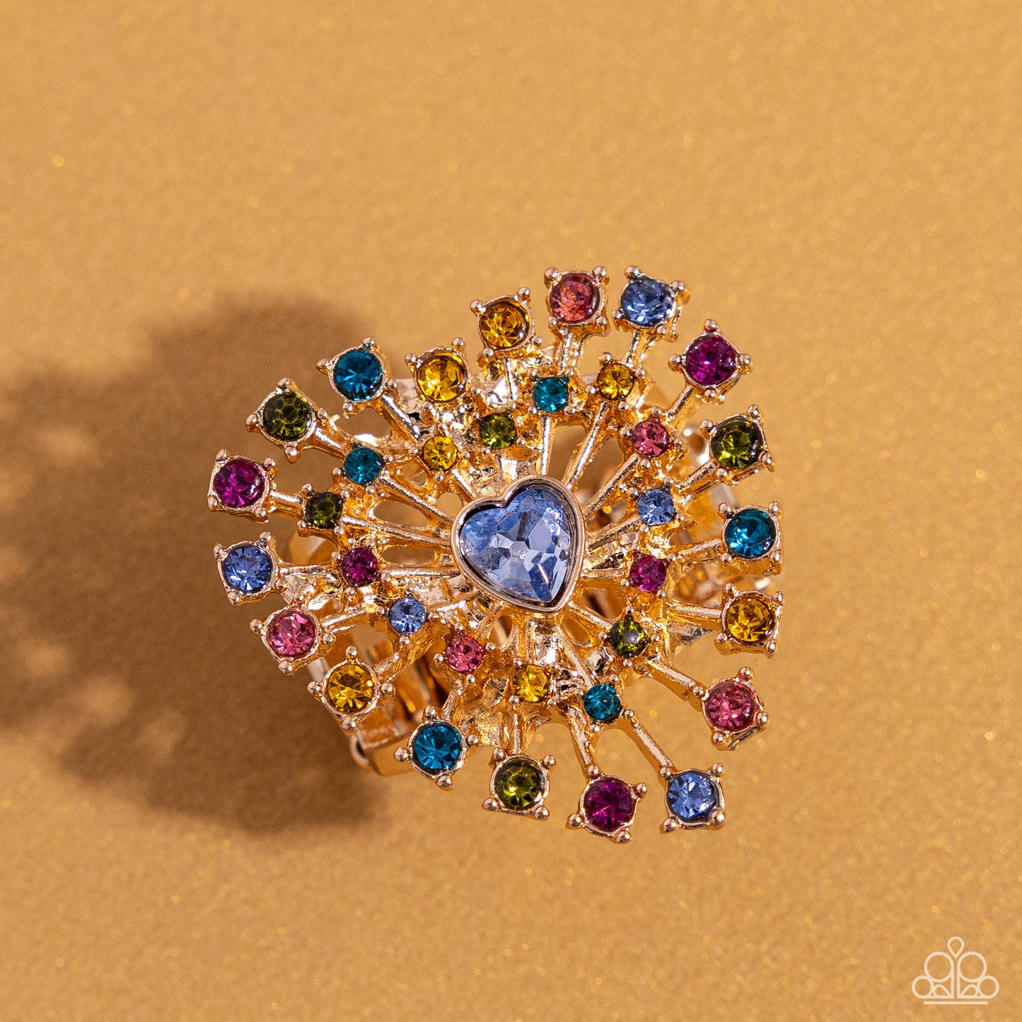 Paparazzi Accessories - Bewitching Beau - January 2024 Life of the Party - Multi Ring set in pronged gold square fittings, multicolored round rhinestones circle a light sapphire heart gem in a sunburst pattern for a bewitching display. Features a stretchy band for a flexible fit. Sold as one individual ring.