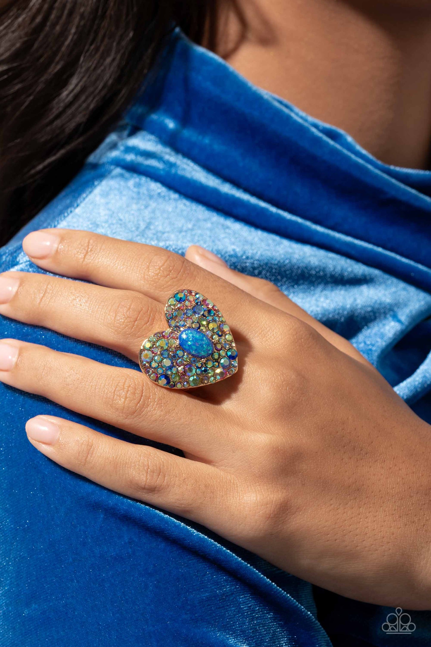 Encrusted in brilliant multicolored and iridescent rhinestones, a glittery gold heart frame adorns the center of an airy gold band for a flirtatious finish. Featuring iridescent flecks, an opalescent blue oval bead is pressed in the center of the heart frame for additional eye-catching shimmer. Features a stretchy band for a flexible fit. Due to its prismatic palette, color may vary. Sold as one individual ring.