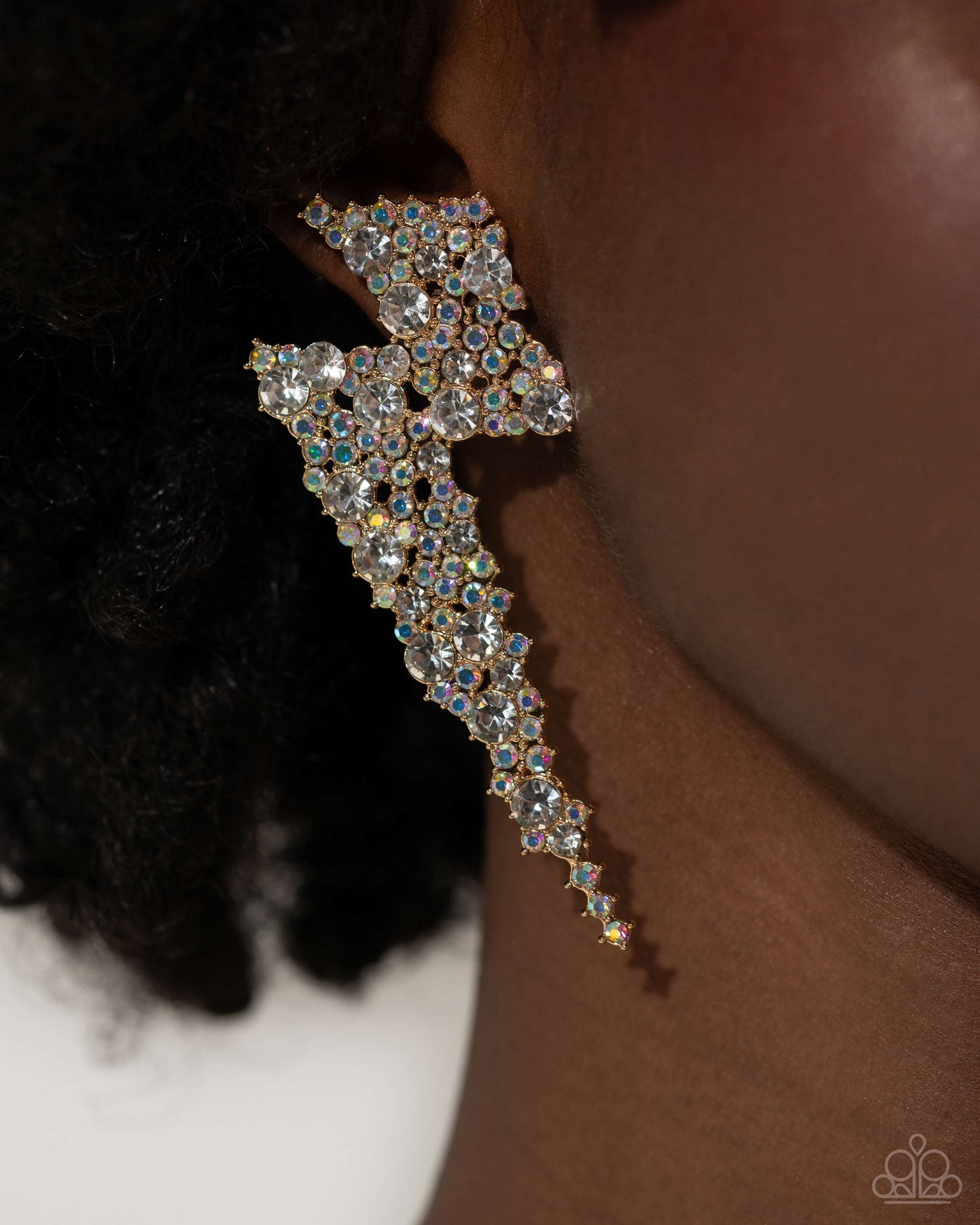 Paparazzi Accessories - Electric Effulgence - Gold Earrings featuring white gems and iridescent rhinestones, a pair of airy gold lightning bolts flicker and flash along the ear for a dazzling design. Earring attaches to a standard post fitting. Due to its prismatic palette, color may vary. Sold as one pair of post earrings.