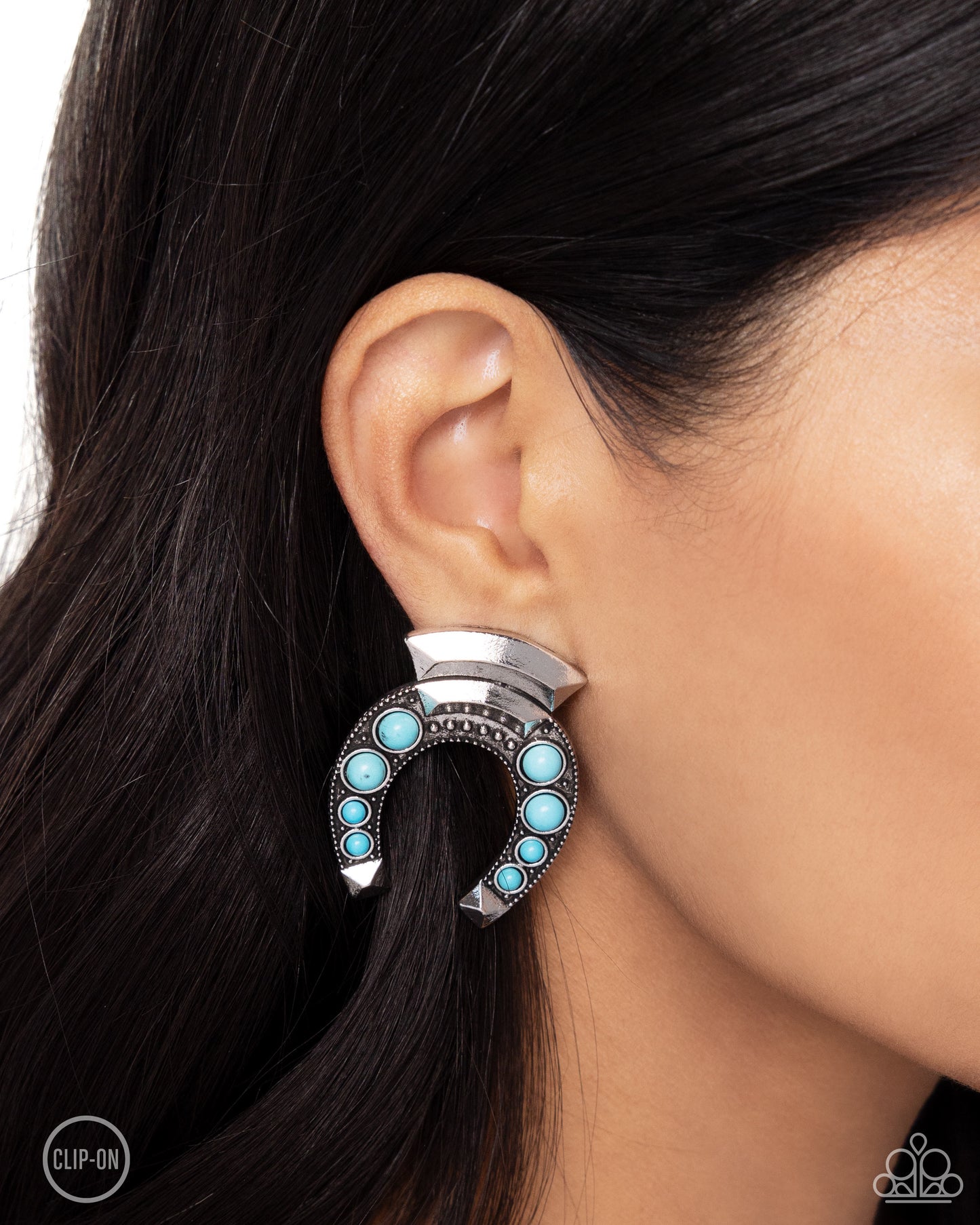 Embellished with turquoise stones and silver-studded details, an oversized antiqued silver horseshoe hangs upside down from a curved high-sheen silver accent. Additional high-sheen textured silver squares that come to a point, cap the ends of the horseshoe for additional eye-catching color. Earring attaches to a standard clip-on fitting. As the stone elements in this piece are natural, some color variation is normal. Sold as one pair of clip-on earrings.