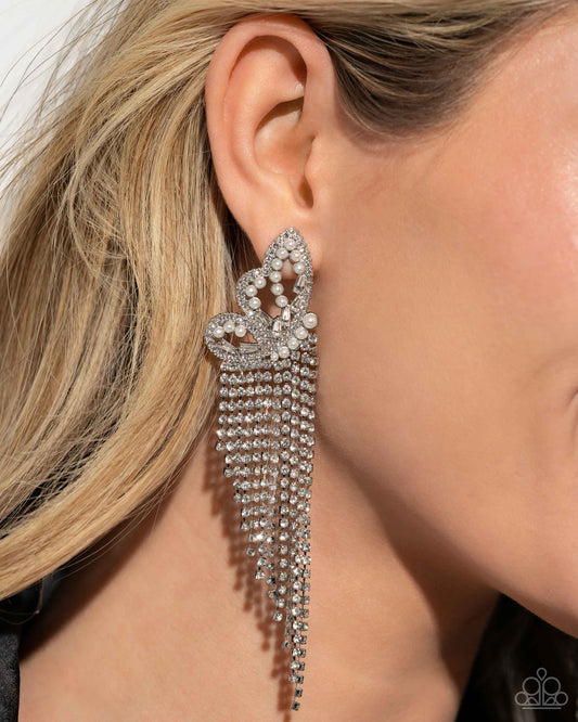 <p>Paparazzi Accessories - Aerial Accent - White Earrings glassy white rhinestones, dainty white pearls, and white emerald-cut gems are encrusted along the front of an airy silver butterfly frame, creating a whimsical centerpiece. Staggered rows of white rhinestones pressed in delicate silver square fittings cascade from the sparkly centerpiece, seemingly lifting the butterfly off to its glitzy flight. Earring attaches to a standard post fitting.</p> <p><i>Sold as one pair of post earrings.</i></p>