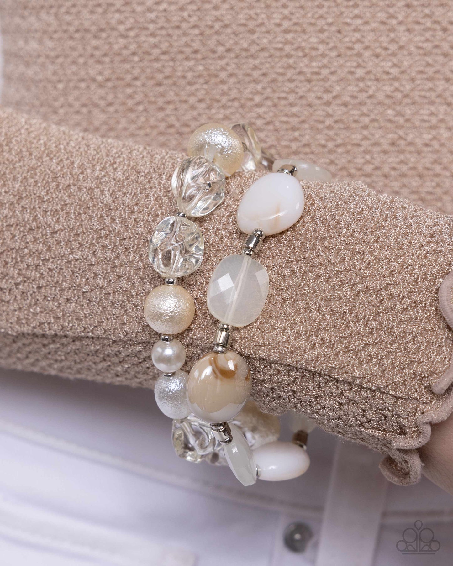 collection of clear, pearl, and textured white and ivory beads combine with silver paperclip chain links, silver beads, ivory beads in various opacities, and brown-swirl patterned reflective beads along the neckline in layers for an everyday elegant look. Features an adjustable clasp closure. Sold as one individual necklace. Includes one pair of matching earrings.
