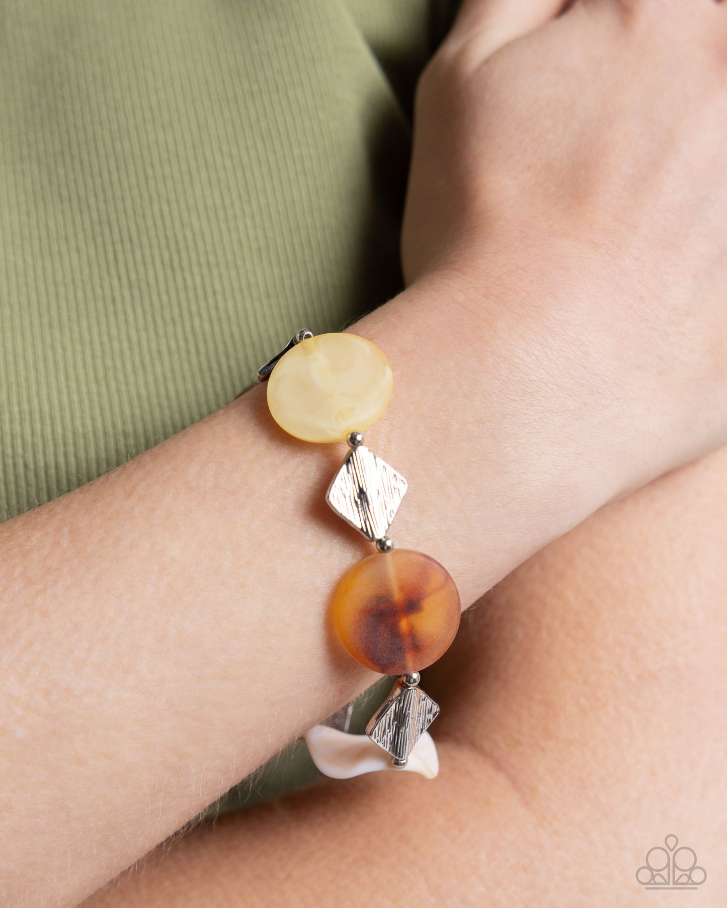 Infused along an elastic stretchy band, a collection of textured diamond silver beads, round silver beads, and clear blue, milky Primrose, brown swirled, and white swirled with brown beads in varying shapes coalesce along the wrist for an artistic, animated look. Sold as one individual bracelet.