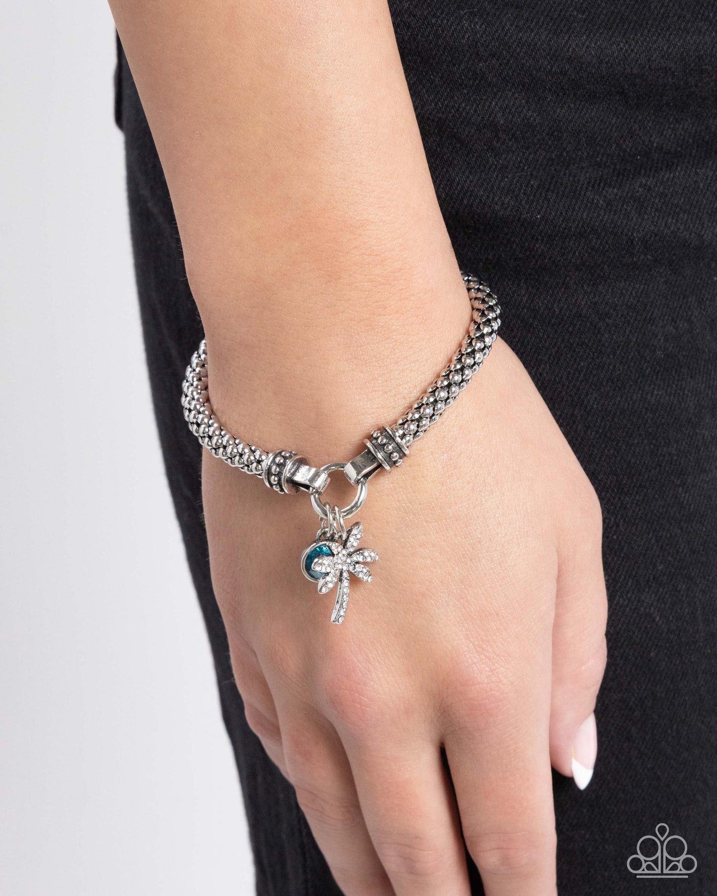 Featuring a high-sheen finish, a rounded silver mesh claw chain streams along the wrist from silver studded caps on a stretchy band. The meshed strand attaches to a silver ring at the center of the wrist where a white rhinestone-encrusted palm tree and solitaire blue zircon gem pressed in a silver fitting swing for a whimsical finish. Sold as one individual bracelet.