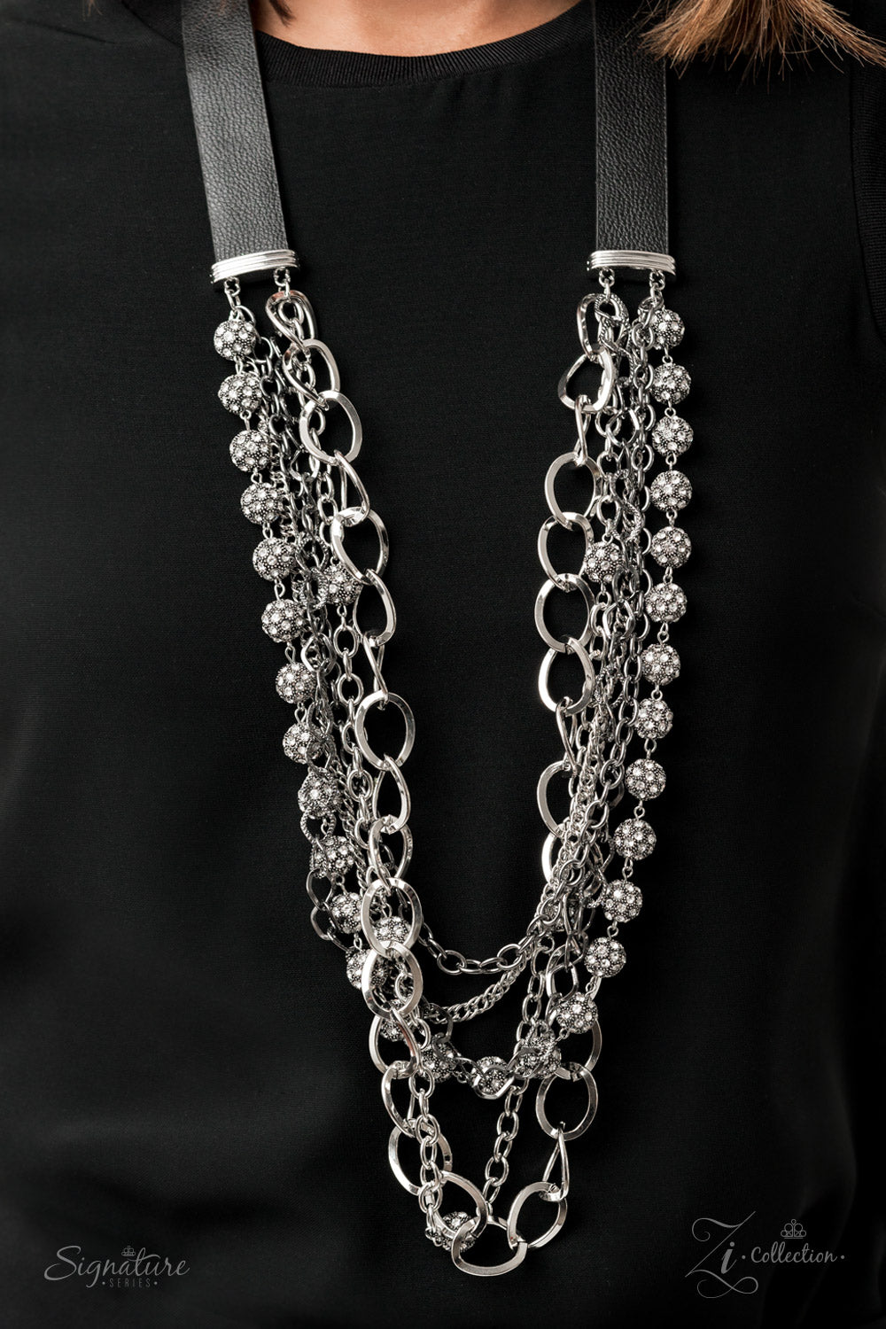 The Arlingto 2020 Zi Collection Necklaces attached to two strips of black leather, strands of bedazzled white rhinestone encrusted silver beads drape between an exaggerated display of mismatched silver and gunmetal chains down the chest. With its edgy sparkle, grunge meets glamour in this heart-stopping statement-maker. Features an adjustable clasp closure. Sold as one individual necklace. Includes one pair of matching earrings.