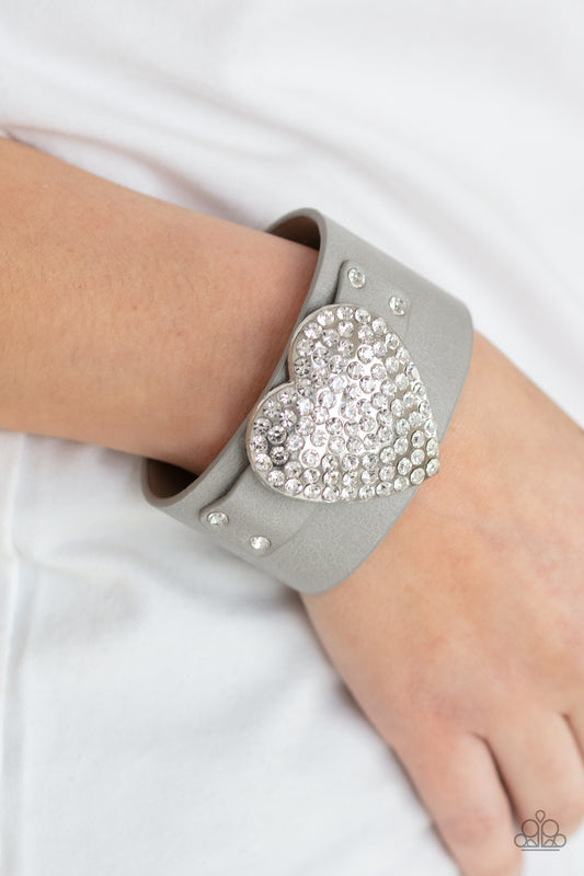 Flauntable Flirt - Silver Bracelets encrusted in blinding white rhinestones, an oversized silver heart frame is studded in place across the front of a gray leather band, creating a flirtatious centerpiece around the wrist. Features an adjustable snap closure.  Sold as one individual bracelet.  Paparazzi Jewelry is lead and nickel free so it's perfect for sensitive skin too!