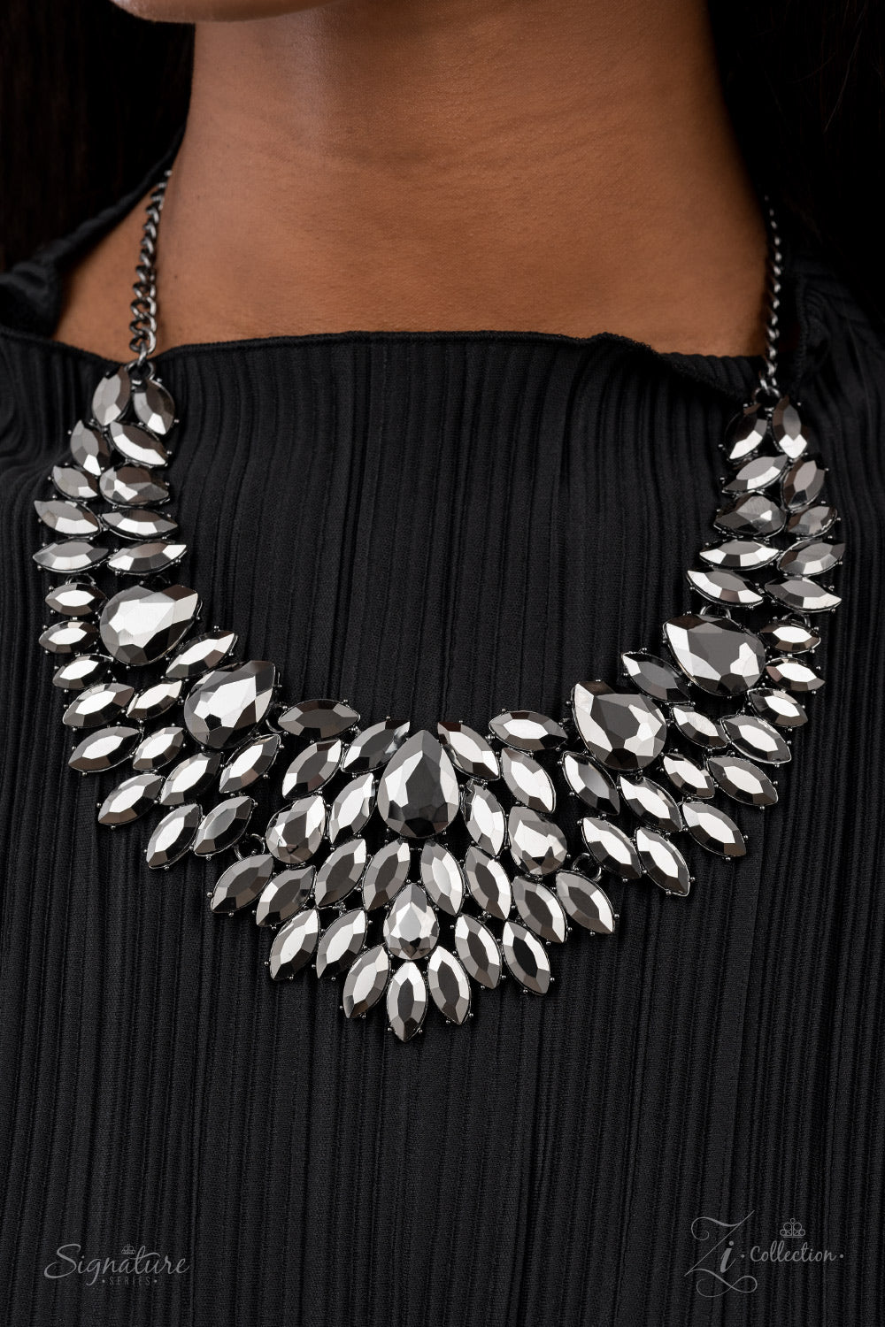 The Tanisha - 2021 Zi Collection Necklace smoldering collection of oversized teardrop and marquise cut hematite rhinestones daringly fan out from the collar, coalescing into intense interconnected frames. The dauntless display of dazzle locks in place, creating a stunningly solitaire sparkle. Features an adjustable clasp closure.  Named after the 2021 Seize the Spotlight winner, Tanisha F.  Sold as one individual necklace. Includes one pair of matching earrings.