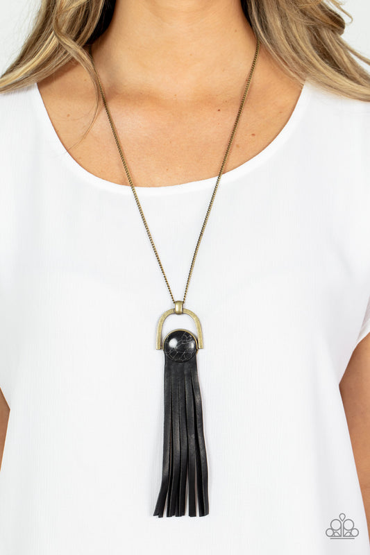 Winslow Wanderer - Brass and Leather Necklaces strips of black leather fan out from the bottom of a round black stone that is threaded along a metal rod that attaches to the bottom of a brass horseshoe frame. The earthy pendant swings from the bottom of an extended brass chain, resulting in a wildly wonderful tassel. Features an adjustable clasp closure.  Sold as one individual necklace. Includes one pair of matching earrings.