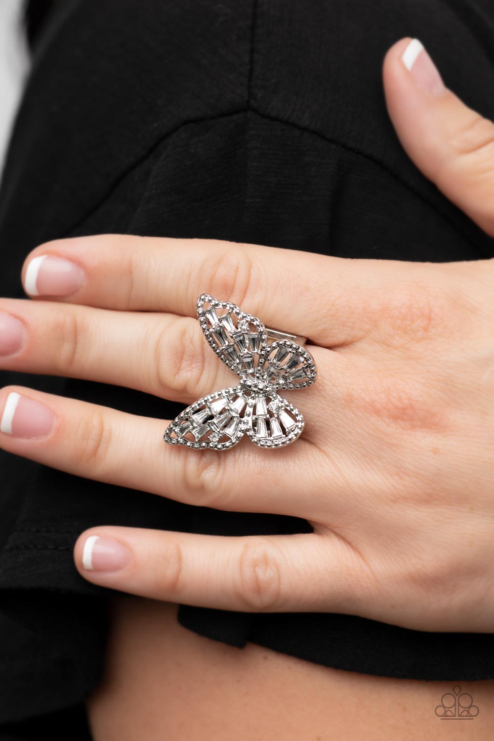 Paparazzi Accessories - Bright-Eyed Butterfly - White Rings a glitzy collection of emerald cut rhinestones are sprinkled across the studded wings of a shiny silver butterfly, resulting in a whimsical centerpiece atop the finger. Features a stretchy band for a flexible fit. Sold as one individual ring.