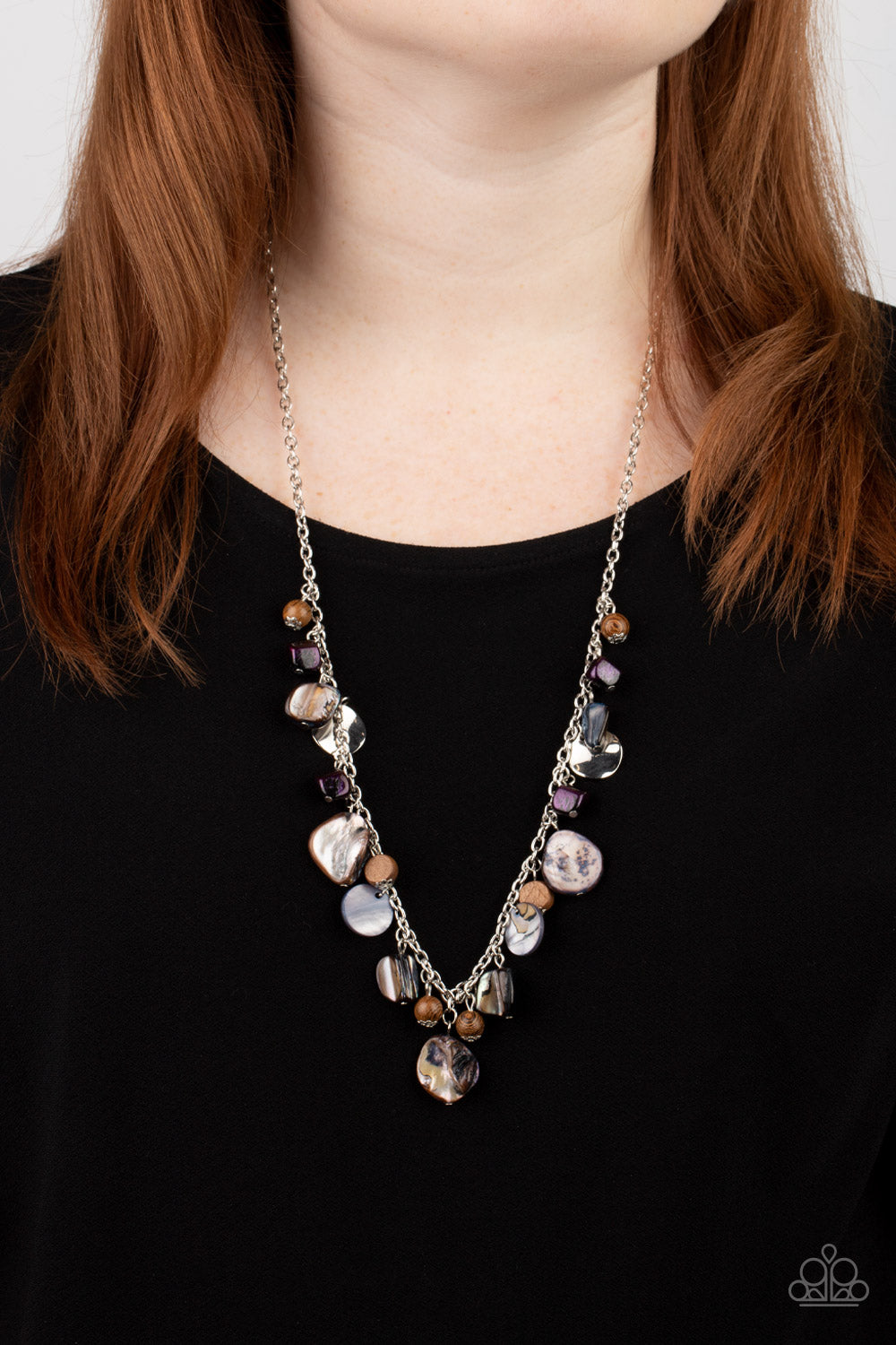 Paparazzi Accessories - Caribbean Charisma - Purple Necklaces a mismatched collection of warped silver discs, brown wooden beads, and iridescent shell-like rock accents dances from the bottom of a classic silver chain, creating a tropical sensation across the chest. Features an adjustable clasp closure.  Featured inside The Preview at GLOW!  Sold as one individual necklace. Includes one pair of matching earrings.