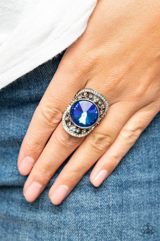 Paparazzi Accessories - Galactic Garden - Blue Gem Ring a dramatically oversized, iridescent blue gem is pressed into the center of an oval silver frame dotted and bordered in glassy white rhinestones, resulting in a sparkly filigree-filled centerpiece atop the finger. Features a stretchy band for a flexible fit. Due to its prismatic palette, color may vary.  Sold as one individual ring.