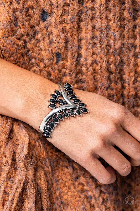 Paparazzi Accessories Teton Tiara - Black Stone Convention Bracelet black oval stones, encased in studded silver frames, line the edge of a daring V-shaped silver cuff. A gathering of black stones adorns the center of the bracelet, adding a finishing touch to the rustically regal cuff.  Sold as one individual bracelet.  2022 Glow Convention