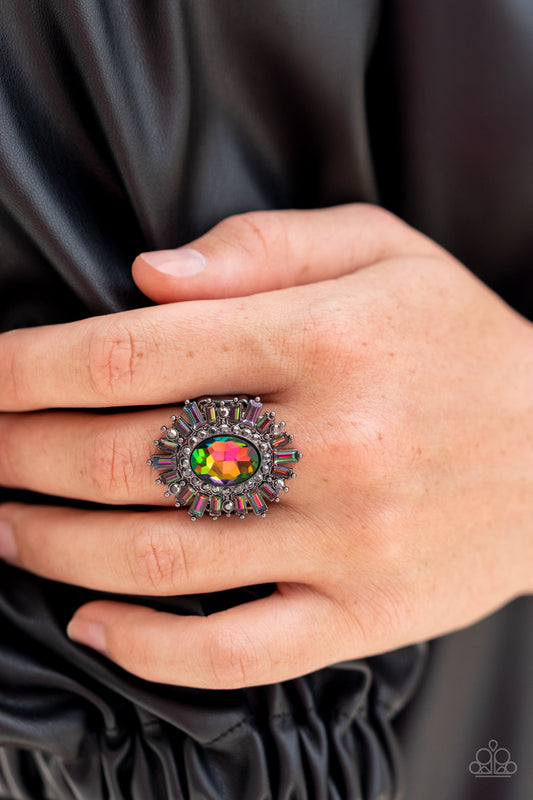 Paparazzi Accessories - Astral Attitude - Multi Oil Spill August 2022 Life of the Party Rings a large oil spill rhinestone sparkles inside a ring of dainty hematite rhinestones. Emerald cut oil spill and hematite rhinestones fan out from the dazzling center, exploding into a stellar centerpiece atop the finger. Features a stretchy band for a flexible fit. Due to its prismatic palette, color may vary.  Sold as one individual ring.
