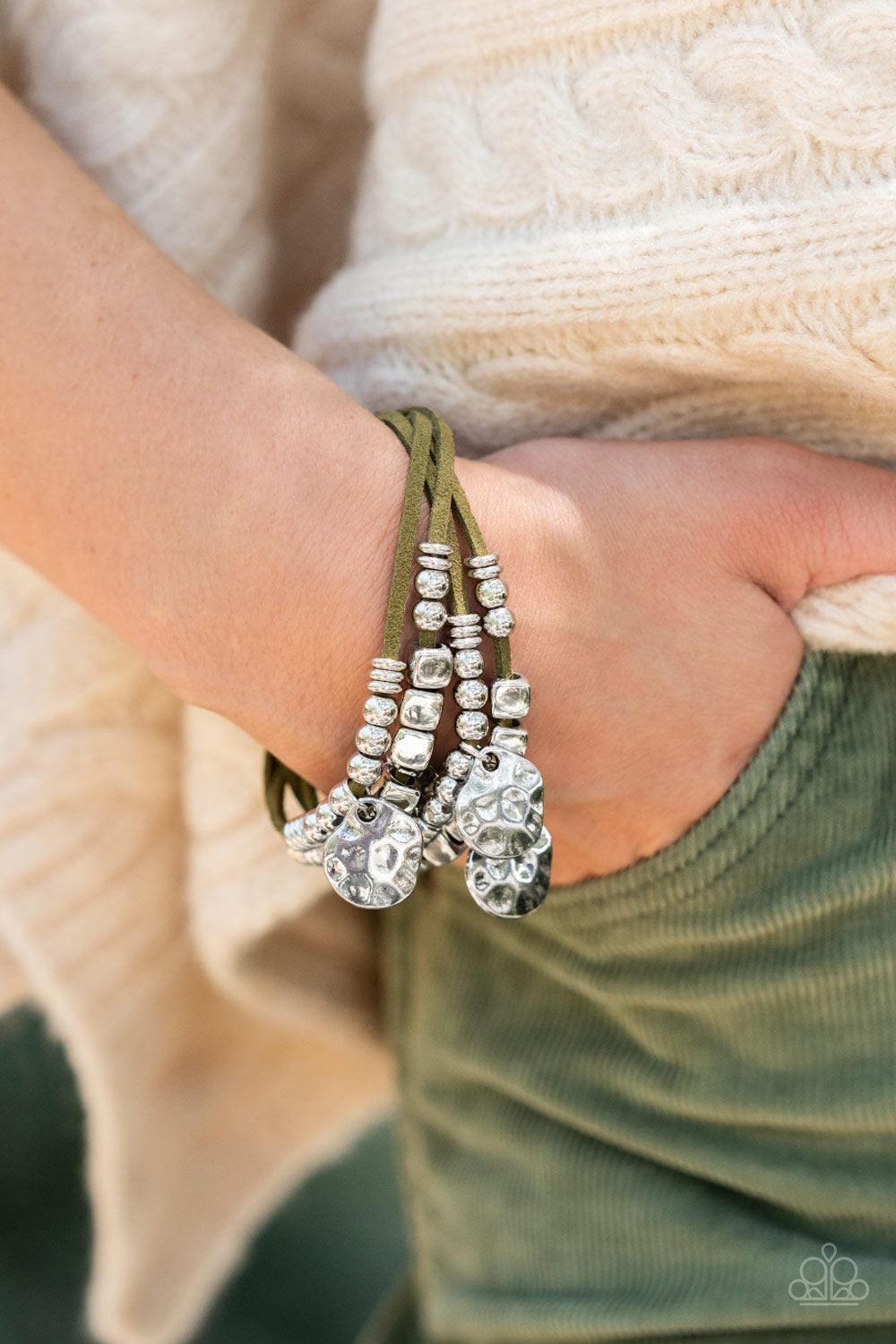Paparazzi Accessories Token Trek - Green Hammered Convention Bracelets asymmetrical, hammered silver discs swing from layers of Martini Olive suede that are adorned with silver discs, beads, and cubes, resulting in noisemaking shimmer around the wrist. Features an adjustable clasp closure. Sold as one individual bracelet. 2022 Glow Convention