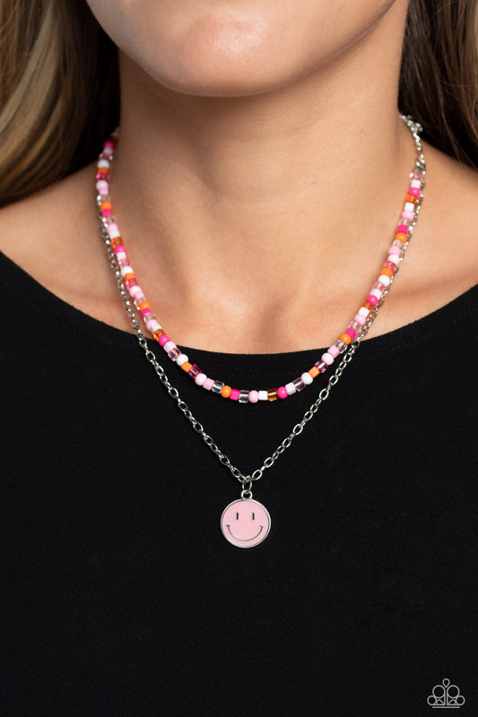 Paparazzi Accessories - High School Reunion - Pink Smiley Necklace Gliding from a dainty, silver chain, a smiley face pendant stands out against a pink backdrop. Completing the charismatic ensemble, a collection of seed beads in shades of light pink, white, pink, orange, and hot pink create bright pops of color around the neckline for a youthful finish. Features an adjustable clasp closure.  Sold as one individual necklace. Includes one pair of matching earrings.