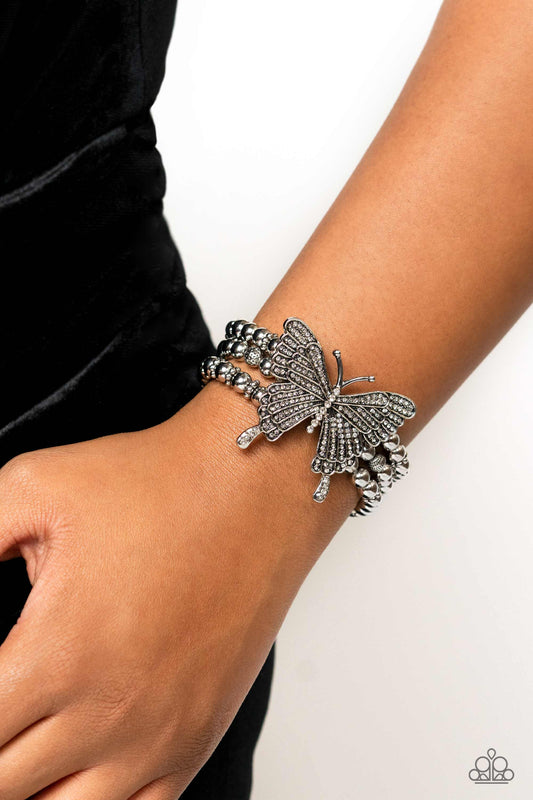 Paparazzi Accessories - First WINGS First - White 2023 EMP Butterfly Bracelets strung along elastic stretchy bands, a trio of silver and textured silver beads and accents wrap around the wrist. Featured atop the beaded collection, an oversized silver butterfly, with intricate details, is sprinkled with dainty white rhinestones across its wings and body, for a dramatically dazzling finish.  Sold as one individual bracelet.