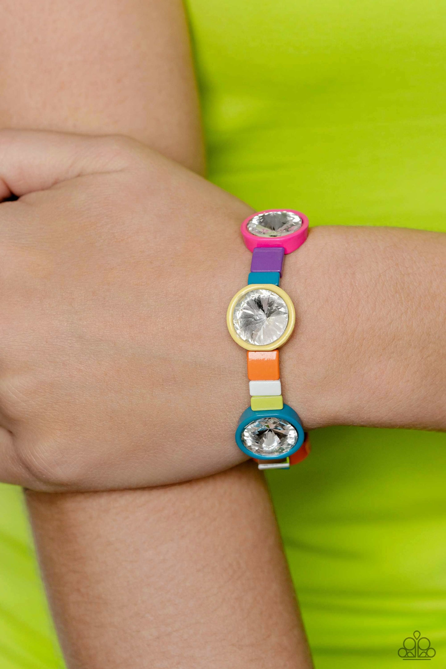 Strung along elastic stretchy bands, a bodacious collection of silver accents, and varying metallic accents dipped in multicolored shades encircle the wrist. Sporadically infused between the colorful display, concaved circular frames in orange, yellow, purple, Pink Peacock, and blue shades feature faceted white gems that come to a point for a touch of sparkle. Sold as one individual bracelet.
