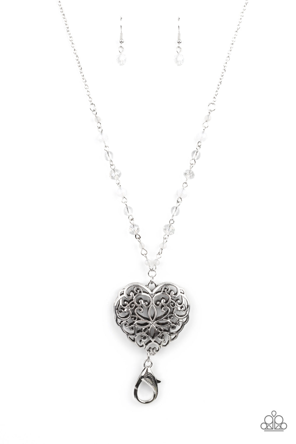 Paparazzi Accessories Doting Devotion - White Lanyard Necklaces a dainty collection of opaque, glassy, and crystal-like beads give way to an oversized filigree filled heart frame, creating an antiqued locket inspired pendant at the bottom of a lengthened silver chain. A lobster clasp hangs from the bottom of the design to allow a name badge or other item to be attached. Features an adjustable clasp closure.