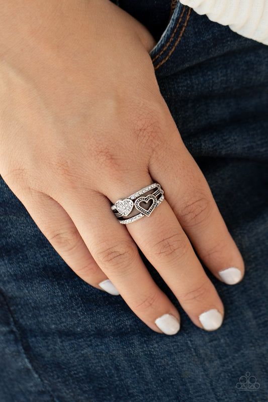 Paparazzi Accessories You Make My Heart BLING - White Rings two rows of white rhinestone encrusted bands flank a dainty silver band dotted in antiqued studs across the finger. A white rhinestone encrusted heart and studded silver heart overlap the layered bands, creating a colorfully charming centerpiece. Features a dainty stretchy band for a flexible fit.