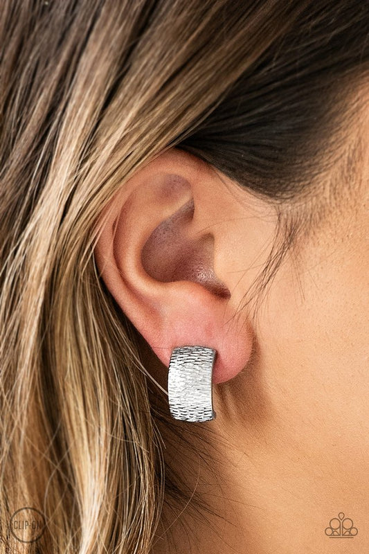 Rippling with tactile textures, a shimmery silver ribbon curls into an edgy frame for a causal look. Earring attaches to a standard clip-on fitting.  Sold as one pair of clip-on earrings.