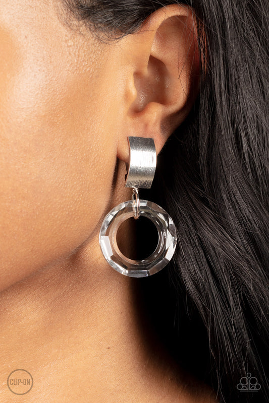 Paparazzi Accessories - Clear Out - White Acrylic Clip-on Earrings a faceted acrylic ring links to the bottom of a curved silver plate, creating a modern lure. Earring attaches to a standard clip-on fitting.  Sold as one pair of clip-on earrings.