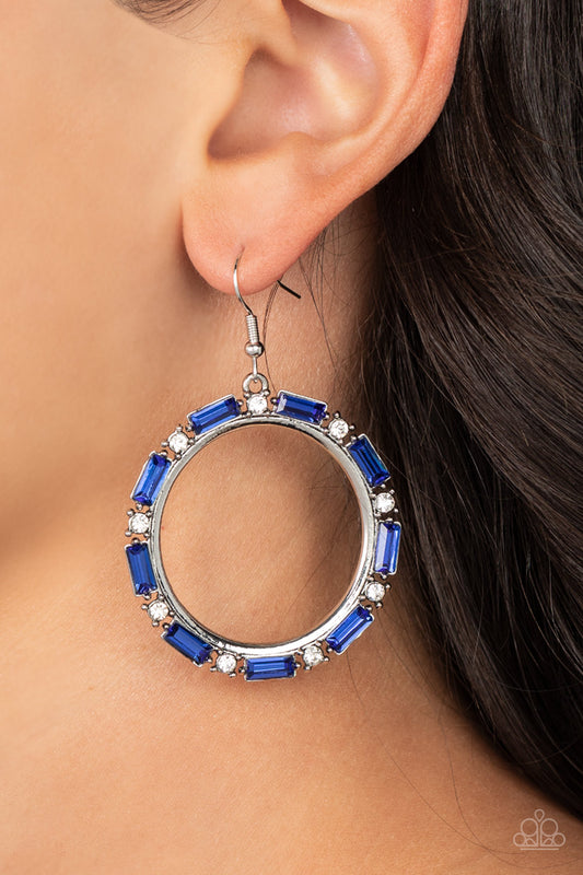 Paparazzi Accessories - Gritty Glow - Blue Rhinestone Earring a glittery collection of round white and emerald cut blue rhinestones smolders along the outside rim of a shiny silver hoop, resulting in an edgy centerpiece. Earring attaches to a standard fishhook fitting.  Sold as one pair of earrings.