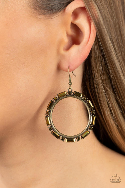 Paparazzi Accessories - Gritty Glow - Brass Earrings a gritty collection of round and emerald cut aurum rhinestones smolders along the outside rim of an antiqued brass hoop, resulting in an edgy centerpiece. Earring attaches to a standard fishhook fitting.  Sold as one pair of earrings.