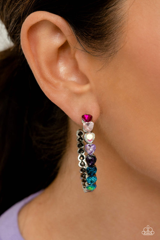 Paparazzi Accessories - Hypnotic Heart Attack - Multi June 2023 LOP Hoop Earrings Featuring a scalloped heart frame, glittery heart rhinestones in shades of pink, iridescence, purple, blue, and a refracted green shimmer slowly decrease in size as they curve down the ear to meet dainty silver hearts for a romantic statement. Earring attaches to a standard post fitting. Hoop measures approximately 1 3/4" in diameter. Due to its prismatic palette, color may vary.  Sold as one pair of hoop earrings.