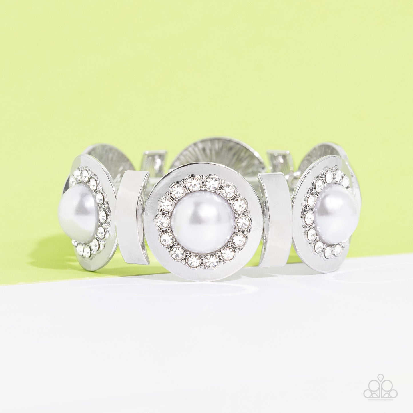 Paparazzi Accessories - Summer Serenade - White Pearl June 2023 LOP Bracelet boncaved silver frames, with an embossed row of white gems, encircle an oversized pearl center creating refined flowers. Sleek curls of silver alternate between the bejeweled flowers for additional shine and capricious shimmer along the wrist on stretchy bands.  Sold as one individual bracelet.