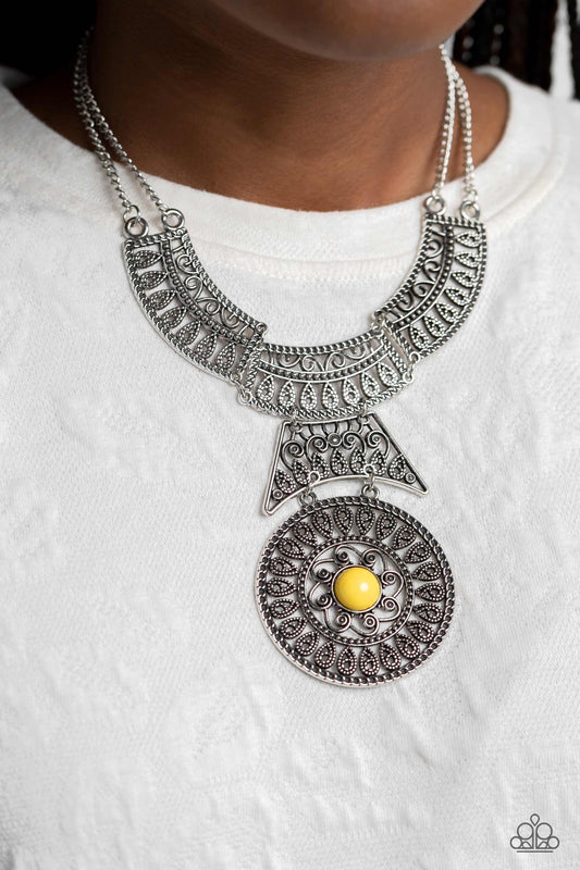 rows of oversized silver filigree frames stack into a crescent-shape that is anchored by additional silver filigree frames that layer down the neckline. Featured in the center of the lowermost circular frame, a glossy yellow bead, creates a hypnotic pendant that swings dramatically. The elaborate statement piece is suspended from a sleek double silver chain, emphasizing the whimsical curls emanating from the design. Features an adjustable clasp closure.  Sold as one individual necklace.