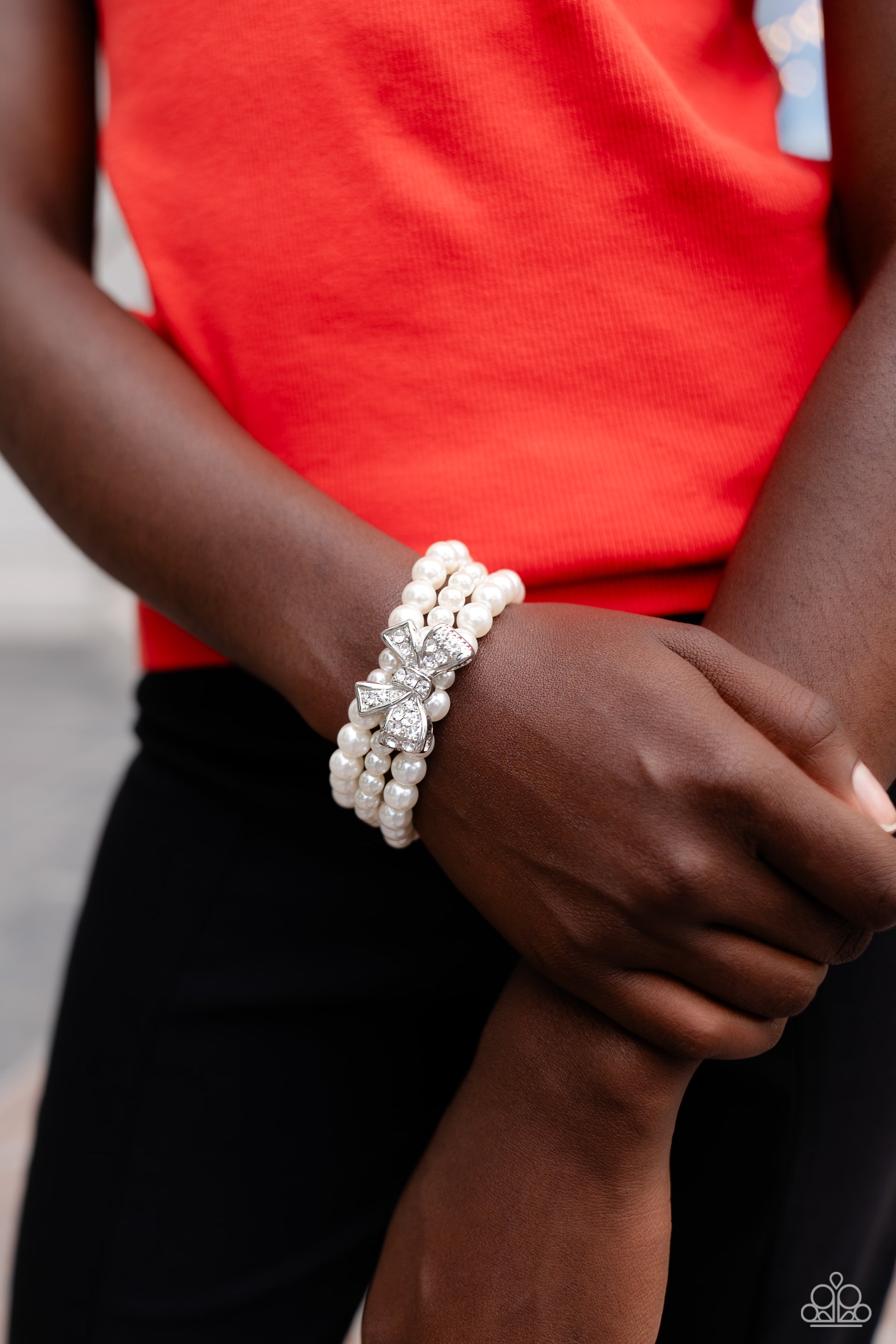 Paparazzi Accessories - How Do You Do? - White Pearl Bracelet strung along elastic stretchy bands, three strands of high-sheen classic white pearls wrap around the wrist. Featured atop the pearly collection, a loopy silver bow, filled with glistening white rhinestones is attached to the center of the wrist for a dramatically dazzling finish.  Sold as one individual bracelet.