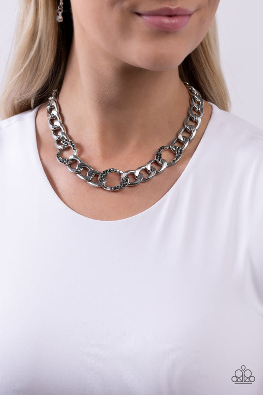 Paparazzi Accessories - Gleaming Harmony - Silver Necklaces dusted in hematite rhinestones, three oblong circle links combine with a strand of bold silver curb chain to drape dramatically across the chest. Features an adjustable clasp closure.  Sold as one individual necklace. Includes one pair of matching earrings.