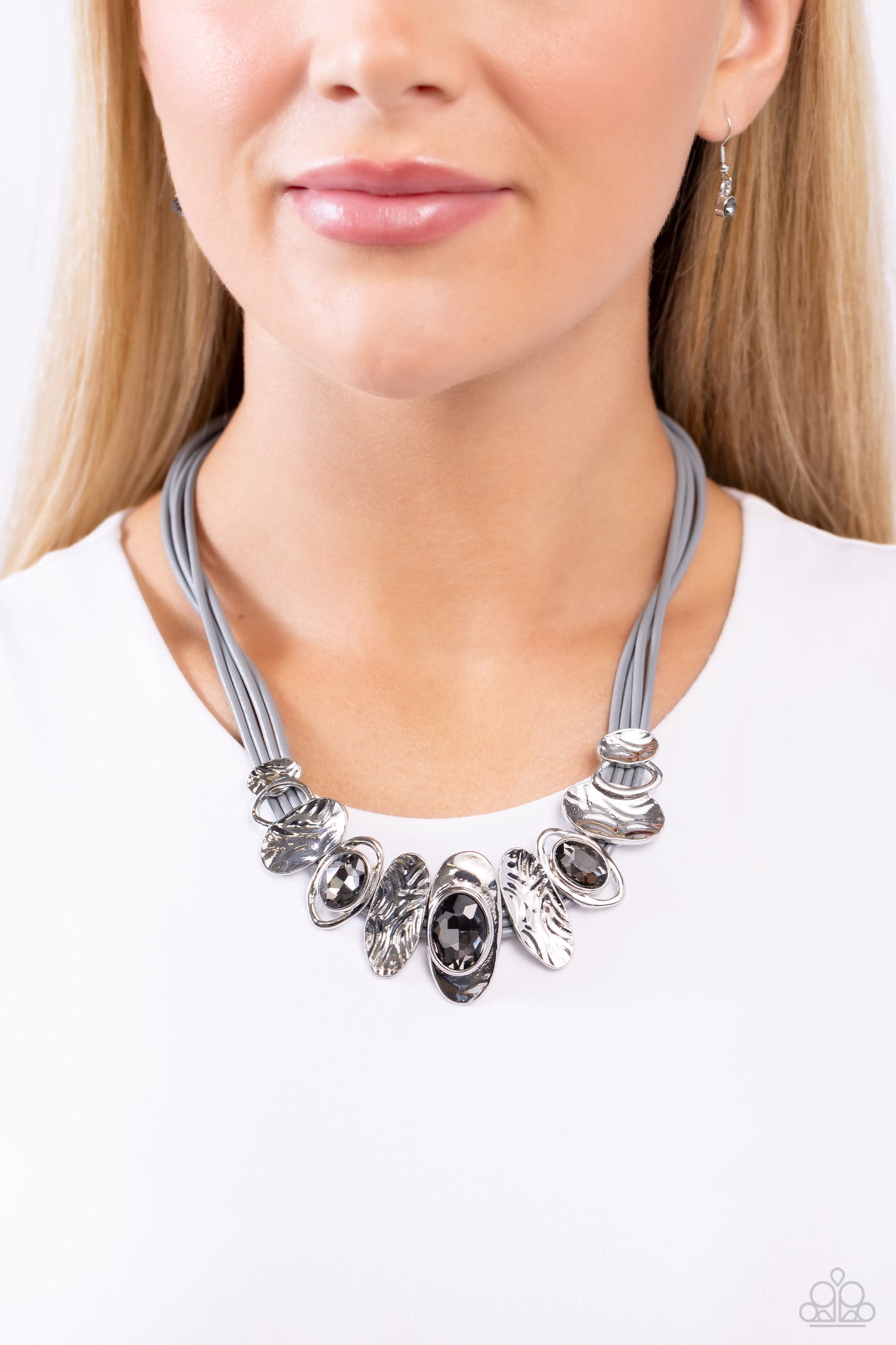 Paparazzi Accessories - Sliding Splendor - Silver Necklaovalfeaturing a lightly hammered sheen, asymmetrical silver ovals, some with airy silhouettes and exaggerated smoky gem centers, give off a hand-made feel as they shift and slide through multiple strands of gray cording for an artisanal design below the collar. Features an adjustable clasp closure.  Sold as one individual necklace. Includes one pair of matching earrings.