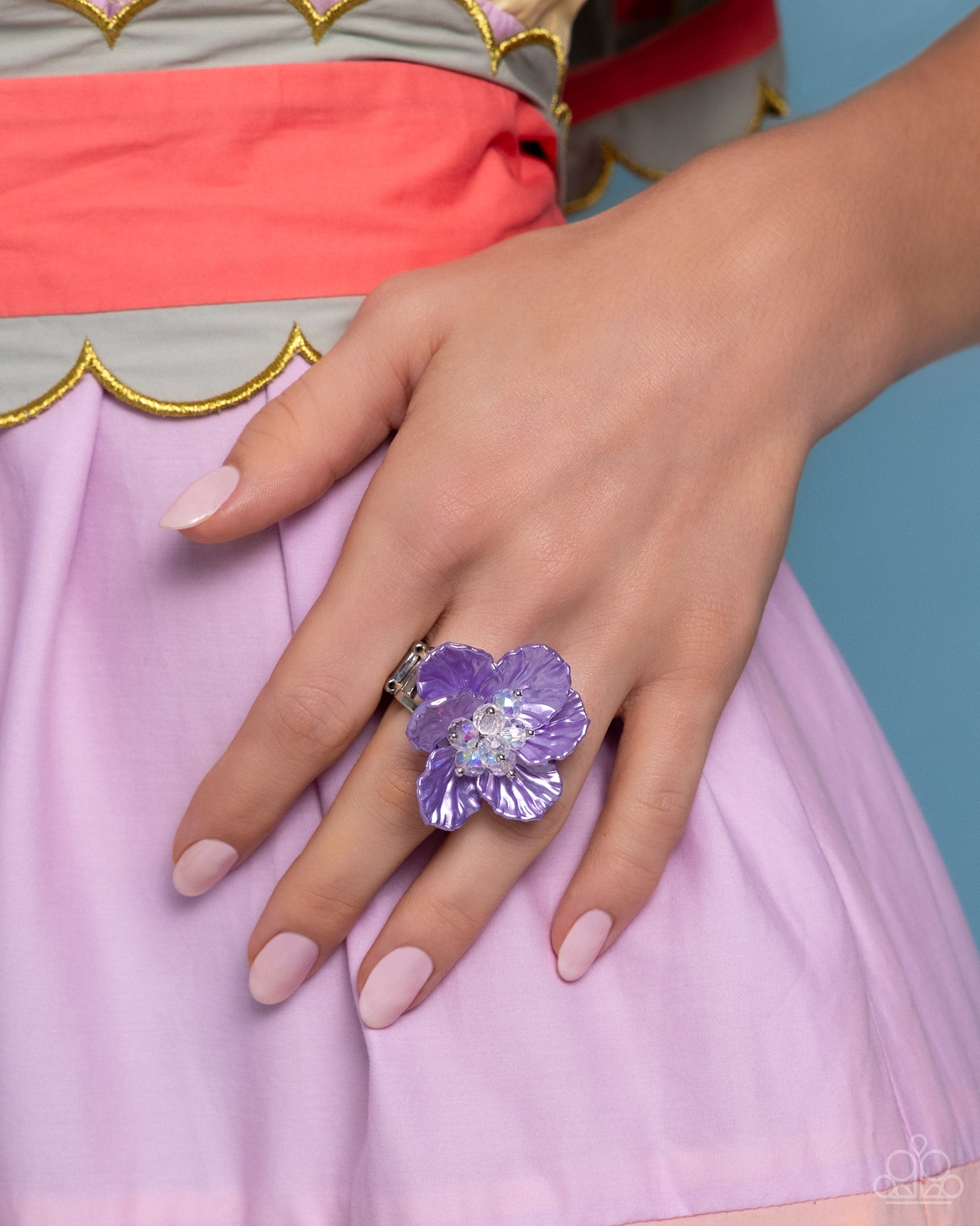 Featuring a warped shell-like texture, an oversized lavender flower glimmers atop the finger for a whimsical finish. Dainty silver studs and clear crystal beads coalesce the center of the flower, adding additional tactile detail. Features a stretchy band for a flexible fit.  Sold as one individual ring.