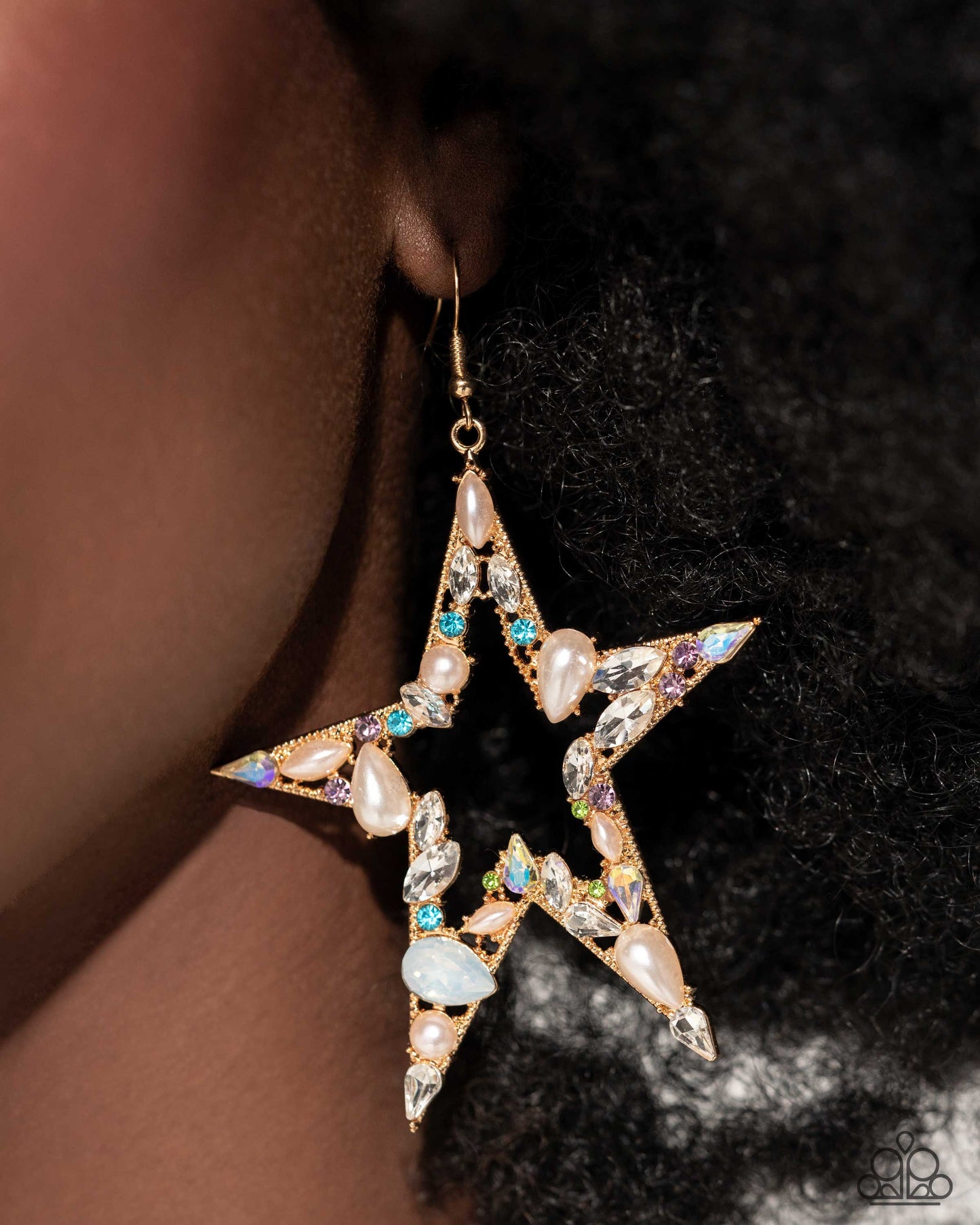 Multicolored rhinestones and gems in various cuts adorn the front of an oversized gold star silhouette, creating a stellar, sparkling centerpiece. Glossy white pearls also in various cuts are sprinkled along the variegated display of shimmer for additional refinement. Earring attaches to a standard fishhook fitting.  Sold as one pair of earrings.