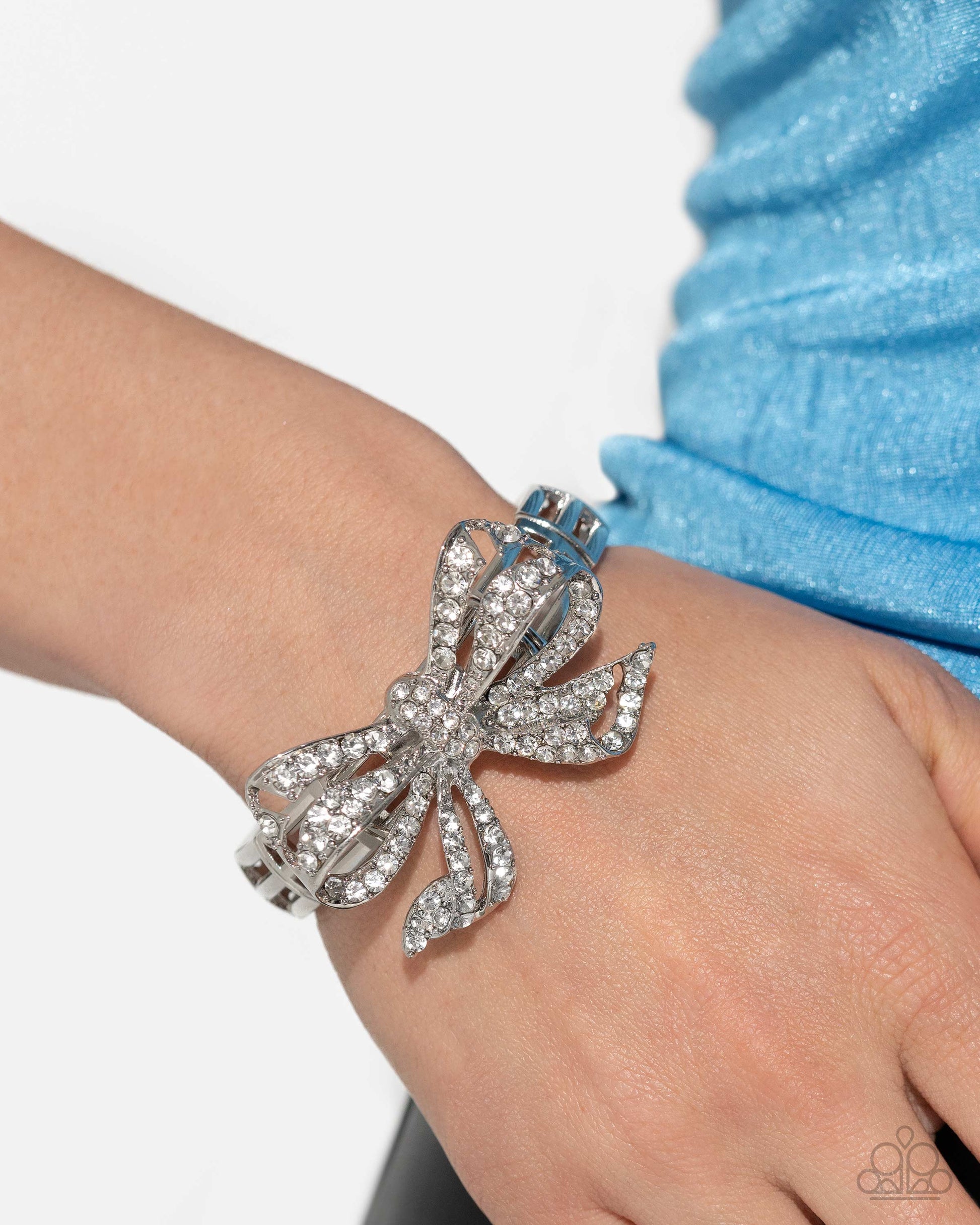 Paparazzi Accessories - It's All A-Bow-t Me - White Bracelets&nbsp;Infused along elastic stretchy bands, airy silver frames gleam along the wrist for a monochromatic display. Encrusted in white rhinestones, an oversized, airy silver bow glitters at the center of the design for a touch of class and refinement.  Sold as one individual bracelet.