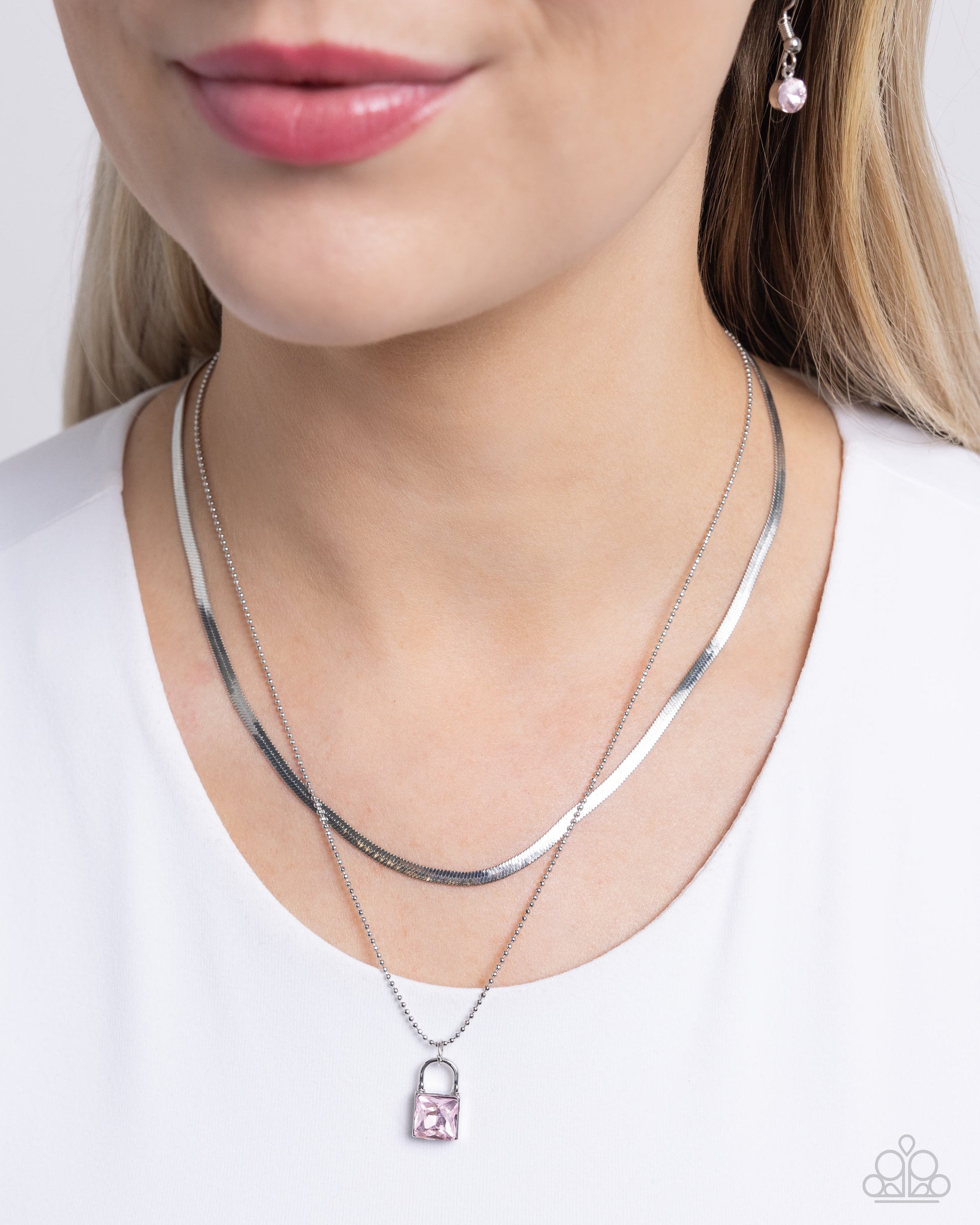 <p data-mce-fragment="1">Pressed in a silver padlock pendant, a square pink gem glistens and glides along a dainty silver ball chain. Layered above the gritty glittery display, a silver herringbone chain creates additional edge and detail. Features an adjustable clasp closure.</p> <p data-mce-fragment="1"><i data-mce-fragment="1">Sold as one individual necklace. Includes one pair of matching earrings.</i></p> <p data-mce-fragment="1"><i data-mce-fragment="1">Order date 4/20/24</i></p>