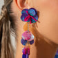 Featuring an iridescent hue, a collection of purple, pink, and orange sequins cascade from a collection of purple sequins that flourish from a hot pink seed beaded starfish for a coastal, chic look. Earring attaches to a standard post fitting. Due to its prismatic palette, color may vary.  Sold as one pair of post earrings.