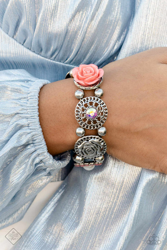 Whimsically woven around the wrist on elastic stretchy bands, a coral resin rose, a silver disc stamped with a paisley motif, an oversized iridescent gem with an orange undertone encased in a textured silver frame, an airy, textured wheel pendant with an iridescent center, a pearl-centered flower with Peach Pink gem petals, and a disc featuring a metallic rose, create a beautifully botanical design. Classic silver beads separate each element, allowing the details of each one to stand out