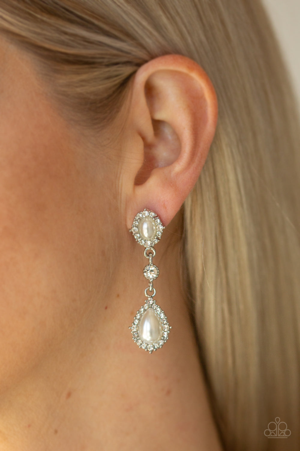 Paparazzi Accessories All-GLOWING - White Earrings solitaire white rhinestone is linked between two pearly white rhinestone encrusted frames, creating an elegant lure. Earring attaches to a standard post fitting.  Sold as one pair of post earrings.