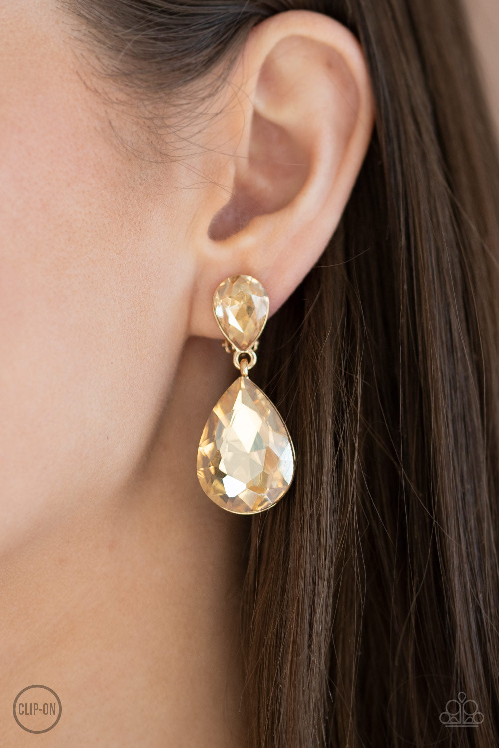 Paparazzi Accessories Aim For the MEGASTARS - Gold Clip-On Earrings dramatically oversized golden rhinestone teardrop swings from the bottom of a smaller rhinestone teardrop, linking into a glamorous lure. Earring attaches to a standard clip-on fitting.  Sold as one pair of clip-on earrings.