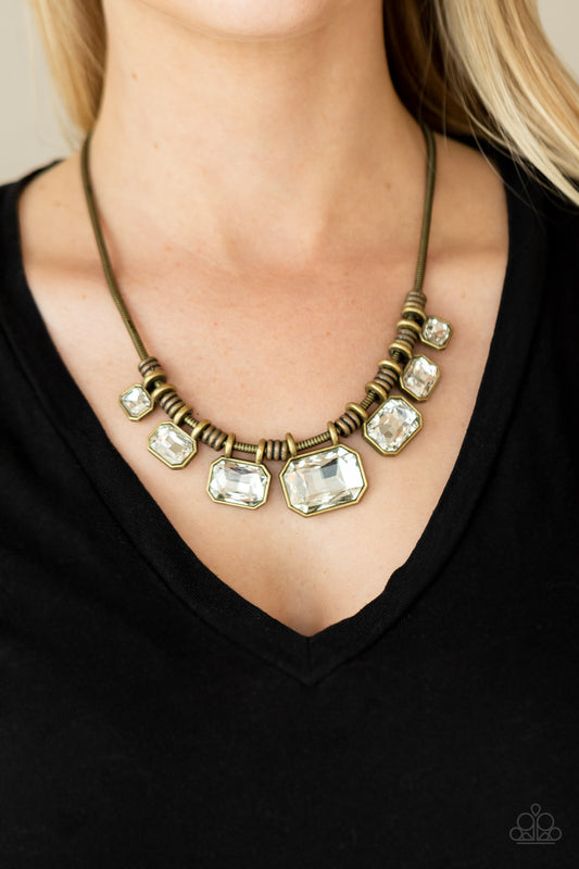 Urban Extravagance - Brass Necklaces featuring regal emerald cuts, white rhinestones gradually increase in size as they glide along a rounded brass snake chain below the collar. Separated by stacks of brass rings, the brilliant rhinestones are encased in matte brass frames for a glamorously gritty finish. Features an adjustable clasp closure.  Sold as one individual necklace. Includes one pair of matching earrings.  Paparazzi Jewelry is lead and nickel free so it's perfect for sensitive skin too!