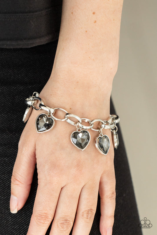 Candy Heart Charmer - Silver Bracelets a smoky heart-shaped gems are encased in sleek silver frames that swing from an oversized silver chain, creating a sparkly fringe around the wrist. Features an adjustable clasp closure.  Sold as one individual bracelet.  Paparazzi Jewelry is lead and nickel free so it's perfect for sensitive skin too!