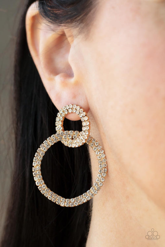 Paparazzi Intensely Icy - Gold Rhinestone Earrings rows of sparkly white rhinestones encircle into two interconnected hoops, creating a jaw-dropping lure. Earring attaches to a standard post fitting.  Sold as one pair of post earrings.